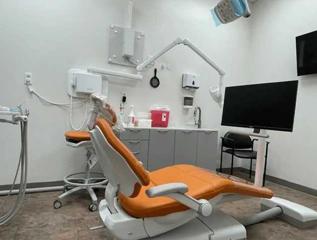 A treatment room at Times Square Family Dental with an orange dental chair and a wall-mounted monitor.